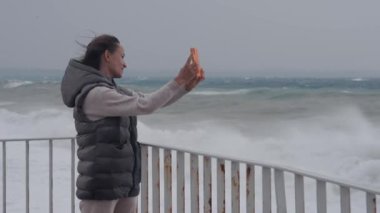 Kız iskelede fırtınada dalgaların arka planında selfie çekiyor..