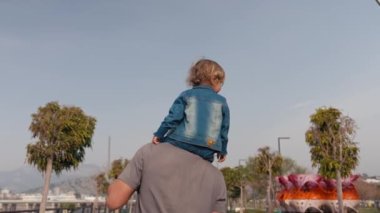 Father and son walking in city at sunset. Two year old kid is sitting on the parents shoulders. Happy family concept. Footage in slow motion. High quality 4k footage