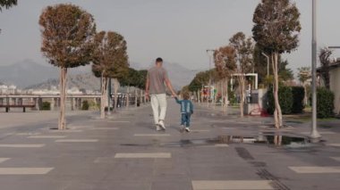 Kafkasyalı genç baba ve oğulun geniş açılı portresi park yolunda geziniyor ve konuşuyor. Dışarıda yürüyen bir adam ve çocuğun portresi. Yeni normal.