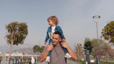 Oğlu babasının omuzlarında oturur, pilotu oynar, süper kahraman olarak uçar. Çocuk yetiştirme konsepti. Mutlu baba ve küçük çocuk oynuyorlar, açık havada rüya görüyorlar. Yüksek kalite 4k görüntü