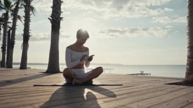 Lotus pozisyonunda oturmuş parkta selfie çeken bir kadın. Sağlık yaşam tarzı meditasyonu. Yüksek kalite 4k görüntü