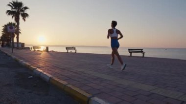 Gün batımında yolda koşan genç bir fitness sporcusu. Sporcu ayakları yolda koşuyor, ağır çekimde. Yüksek kalite 4k görüntü