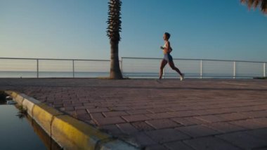 Koşan kadın sporcu gün batımı plajında koşuyor. Güzel bir gün batımında deniz kenarında antrenman yapan spor koşucusu bir kız ya da yazın tüm vücut uzunluğuyla gün doğumunda. Yavaş bir hareket yap. Yüksek kalite 4k görüntü