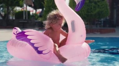 Mutlu şirin çocuk annesiyle yüzme havuzunda şişme flamingoda oturuyor. Ailesi yazın eğleniyor. Yüksek kalite 4k görüntü