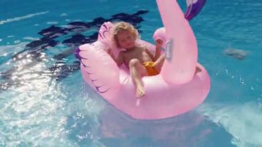 Mutlu şirin çocuk annesiyle yüzme havuzunda şişme flamingoda oturuyor. Ailesi yazın eğleniyor. Yüksek kalite 4k görüntü