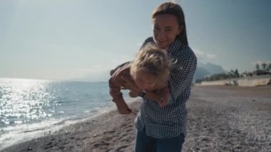Genç bir annenin otantik yakın çekimi kollarını tutarak tatil tatili sırasında deniz kenarında bir plajda küçük bir bebekle oynamaktır. Yüksek kalite 4k görüntü
