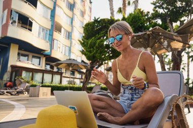 Havuz başında dizüstü bilgisayar kullanan hippi bir kadın. Genç kız havuz kenarında tatildeyken dizüstü bilgisayarda çalışıyor. Yüksek kalite fotoğraf