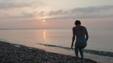 Gün batımında deniz kıyısında koşan spor elbiseli genç bir kadın. Yavaş çekim. Şortlu ve tanklı kız. Mutluluk ve özgürlük kavramı. Yüksek kalite 4k görüntü