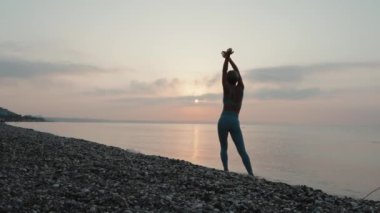 Gün batımında deniz kıyısında koşan spor elbiseli genç bir kadın. Yavaş çekim. Şortlu ve tanklı kız. Mutluluk ve özgürlük kavramı. Yüksek kalite 4k görüntü