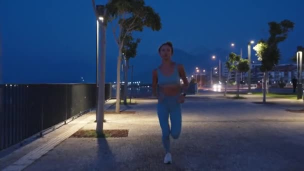 ブルーアスレチックトップで美しいボインのフィットネスガールとストリートでジョギング 彼女は夜にワークアウトをしている 高品質の4K映像 — ストック動画