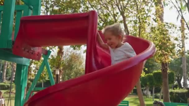 子供は暑い夏の日に公園でグリッドを登ります 多階建ての建物と近代的な住宅複合体の近代的な遊び場の小さな子供のためのロープのスライド — ストック動画