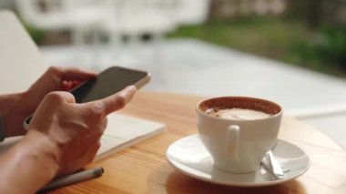 İnternet 'e göz atmak için akıllı telefon kullanan, kafede masada otururken okuyup mesajlaşan serbest çalışan bir kadın. Yaşam tarzı, kahve dükkanında çalışmak. Sosyal medya. Yüksek kalite 4k görüntü