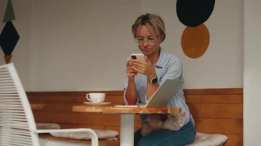 İnternet 'e göz atmak için akıllı telefon kullanan, kafede masada otururken okuyup mesajlaşan serbest çalışan bir kadın. Yaşam tarzı, kahve dükkanında çalışmak. Sosyal medya. Yüksek kalite 4k görüntü