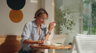 İnternet 'e göz atmak için akıllı telefon kullanan, kafede masada otururken okuyup mesajlaşan serbest çalışan bir kadın. Yaşam tarzı, kahve dükkanında çalışmak. Sosyal medya. Yüksek kalite 4k görüntü