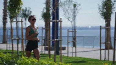 Sıska sarışın kadın gezinti güvertesinde koşuyor, şehir binaları arka planda. Sportif seksi kadın koşuyor, gün batımında dışarıda egzersiz yapıyor. Aktif yaşam tarzı, arka plan. Yüksek kalite 4k görüntü