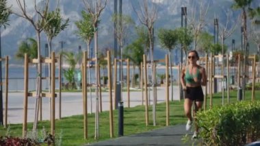 Sıska sarışın kadın gezinti güvertesinde koşuyor, şehir binaları arka planda. Sportif seksi kadın koşuyor, gün batımında dışarıda egzersiz yapıyor. Aktif yaşam tarzı, arka plan. Yüksek kalite 4k görüntü