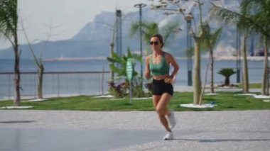 Sıska sarışın kadın gezinti güvertesinde koşuyor, şehir binaları arka planda. Sportif seksi kadın koşuyor, gün batımında dışarıda egzersiz yapıyor. Aktif yaşam tarzı, arka plan. Yüksek kalite 4k görüntü