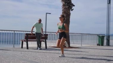 Sıska sarışın kadın gezinti güvertesinde koşuyor, şehir binaları arka planda. Sportif seksi kadın koşuyor, gün batımında dışarıda egzersiz yapıyor. Aktif yaşam tarzı, arka plan. Yüksek kalite 4k görüntü