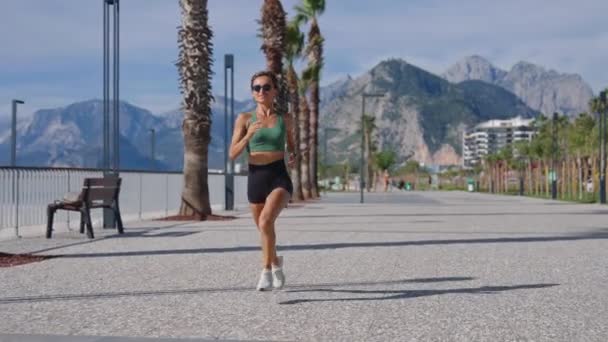 Smal Ung Blond Kvinna Joggar Strandpromenaden Stadsbyggnader Bakgrunden Sportig Sexig — Stockvideo