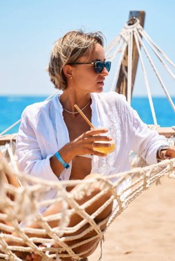 Yaz tatilinin tadını çıkarıyorum. Genç mutlu kadın gün batımında kumlu sahilde hamakta uzanırken dinleniyor. Seyahat konsepti. Yüksek kalite fotoğraf