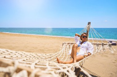 Yaz tatilinin tadını çıkarıyorum. Genç mutlu kadın gün batımında kumlu sahilde hamakta uzanırken dinleniyor. Seyahat konsepti. Yüksek kalite fotoğraf