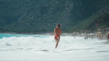 Yazın güneşli bir günde kumsalda atlayan sarı bikinili güzel bir kadın. Güneşli bir günde kumsalda zıplayan güzel bir kadının yan görüntüsü. Sıska kızın seksi sırtı, temiz.. 