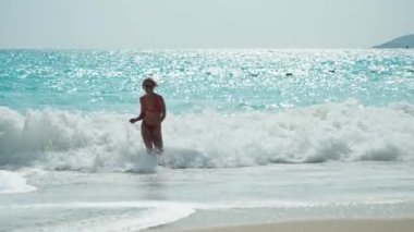 Yazın güneşli bir günde kumsalda atlayan sarı bikinili güzel bir kadın. Güneşli bir günde kumsalda zıplayan güzel bir kadının yan görüntüsü. Sıska kızın seksi sırtı, temiz.. 