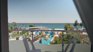 Kadın perdeleri açar ve sabah güzel deniz manzarasına hayran olmak için balkona çıkar. Tatil, Seyahat, Yaz Tatili Turizmi, Deniz Manzaralı Lüks Tatil Köyünde Dinlenme. 