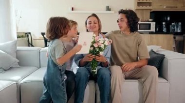 Üç çocuk anneler gününü annelerine çiçek ve tebrik kartı vererek kutluyor. Etrafı sevgi ve sevinçle çevriliyken gülümsüyor. Annelik ve aile bağı kavramı. Orta menzilli atış