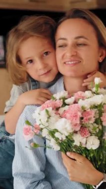 Genç çocuk sıcak ve rahat bir ortamda annesine bir buket çiçek verir. Sevinç ve minnettarlıkla gülümsüyor. Anneler Günü kutlaması ve aile sevgisi kavramı. Orta menzilli doğal ışık