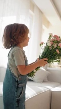 Genç çocuk sıcak ve rahat bir ortamda annesine bir buket çiçek verir. Sevinç ve minnettarlıkla gülümsüyor. Anneler Günü kutlaması ve aile sevgisi kavramı. Orta menzilli doğal ışık