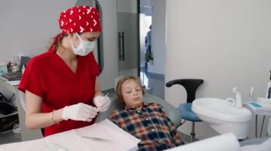 Dişçi muayenehanesinde ultrasonik diş temizliği alan bir çocuğun yakın çekimi. İki diş hekimi dikkatli çalışır, maske ve eldiven giyerler. Pediatrik dişçilik ve diş bakımı kavramı