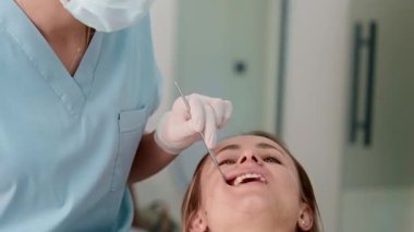 Genç bayan dişçi, modern, parlak bir diş kliniğinde bir kadın hastayı tedavi ediyor. Hasta sandalyede yatarken profesyonelce aletler kullanıyor. Kadın sağlık hizmetleri kavramı ve
