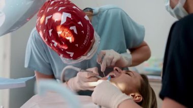 Genç bayan dişçi, modern, parlak bir diş kliniğinde bir kadın hastayı tedavi ediyor. Hasta sandalyede yatarken profesyonelce aletler kullanıyor. Kadın sağlık hizmetleri kavramı ve