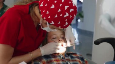 Dişçi muayenehanesinde ultrasonik diş temizliği alan bir çocuğun yakın çekimi. İki diş hekimi dikkatli çalışır, maske ve eldiven giyerler. Pediatrik dişçilik ve diş bakımı kavramı