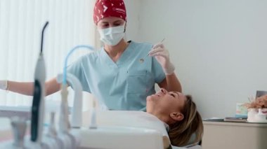 Genç bayan dişçi, modern, parlak bir diş kliniğinde bir kadın hastayı tedavi ediyor. Hasta sandalyede yatarken profesyonelce aletler kullanıyor. Kadın sağlık hizmetleri kavramı ve