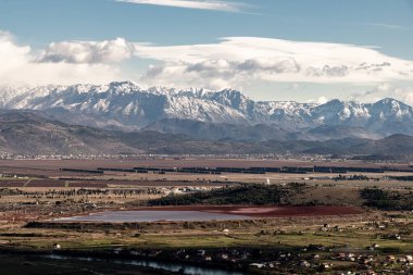 Panoramik bir manzara karla kaplı bir dağ silsilesini küçük evler ve tarlalarla kaplı bir vadiye karşı sergiliyor. Engebeli dağlar ve kırsal manzaralar arasındaki zıtlık bölgenin doğal güzelliğini vurguluyor..