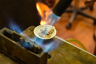 Metal halkalar ve meşale aleviyle ısıtılan diğer gümüş parçalarla eritme kabının yakın çekimi. Yoğun ısı metalin erimesine neden olur ve mücevher dökmek için erimiş bir temel oluşturur..