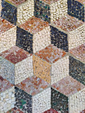 Canlı bir mozaik zemin, karmaşık bir 3 boyutlu küp şeklini gösteriyor. Küçük, çok renkli taşlardan yapılmış. Bu görsel olarak bağlanan tasarım, derinlik ve boyut illüzyonu yaratmak için düzenlenmiş toprak ve nötr renkleri birleştirir..