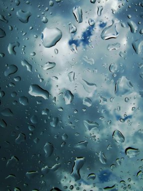 Close-up of raindrops on a glass surface with a dark, cloudy sky in the background. The reflection and shape of each droplet create an abstract and moody scene, capturing the essence of a rainy day. clipart