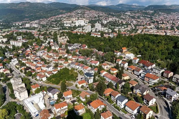 Arka planda yemyeşil bir manzara ve tepelerin olduğu banliyö mahallesinin manzaralı bir manzarası. Doğayla uyum içinde yaşayan, gayrimenkul, yaşam tarzı ve çevre konularına uygun konutları gösteren gösteriler.