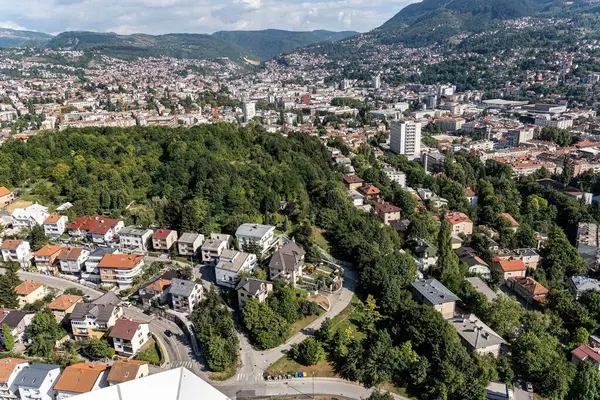 Arka planda yemyeşil bir manzara ve tepelerin olduğu banliyö mahallesinin manzaralı bir manzarası. Doğayla uyum içinde yaşayan, gayrimenkul, yaşam tarzı ve çevre konularına uygun konutları gösteren gösteriler.