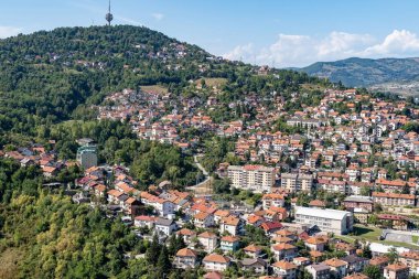 Kırmızı çatılı evleri, yemyeşil yeşillikleri ve tepenin üstünde bir telekomünikasyon kulesi olan pitoresk bir yamaç kasabası. Kenar mahallelerdeki yaşamı, gayrimenkulleri ya da şehir ortamlarındaki doğayı resmetmek için mükemmel..