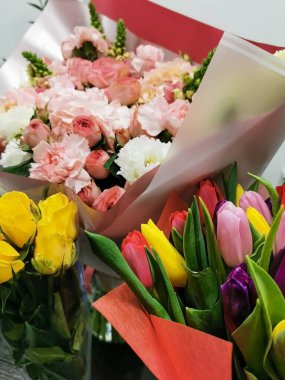 Canlı kağıtlara sarılmış güller, laleler ve karanfillerden oluşan renkli buketler. Kapalı alan, bahar için uygun, kutlamalar, ya da hediye teması.