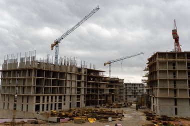 İki kule vinci ve dramatik bulutlu gökyüzünün altında tamamlanmamış beton binası olan modern bir inşaat alanı. Kentsel gelişim, mimari ve altyapı projelerini resmetmek için ideal resim.