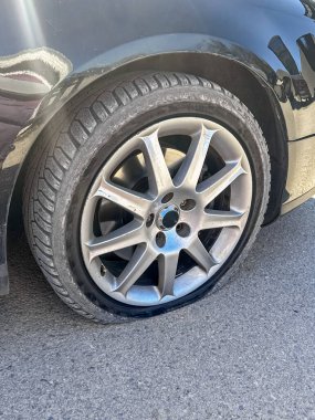 Şehir caddesinde park edilmiş siyah bir arabanın ön lastiği patlamış. Sönük tekerleğe yakın çekim. Araba arızalarını, araba tamirlerini, trafik kazalarını ve şehir içi araç sorunlarını resmetmeye elverişli.