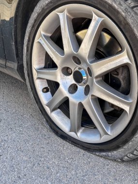 Şehir caddesinde park edilmiş siyah bir arabanın ön lastiği patlamış. Sönük tekerleğe yakın çekim. Araba arızalarını, araba tamirlerini, trafik kazalarını ve şehir içi araç sorunlarını resmetmeye elverişli.