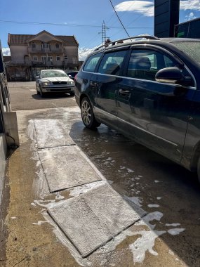 Oto yıkamada siyah bir araba görünür köpük ve suyla yıkanmış. Olay yeri günlük araç bakımını yakalıyor. Temizlik, ulaşım ya da kentsel yaşam tarzı konuları için mükemmel.