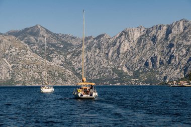 Kotor Körfezi 'nin mavi sularında dramatik kireçtaşı dağları tarafından desteklenen iki yelkenli tekne süzülüyor. Yelkencilik, turizm, Karadağ tanıtımı ve açık hava eğlence temaları için harika.