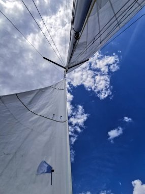 Yelkenli direğinin yukarı görüntüsü ve dağınık bulutlu mavi gökyüzüne karşı yelken açmak. Özgürlük, yelken, macera, seyahat, deniz teması ve deniz yaşam tarzı kavramları için idealdir.